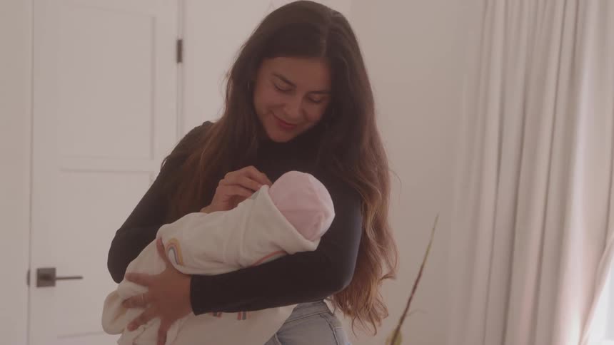 Woman holding a baby wrapped in a white blanket with rainbow patterns