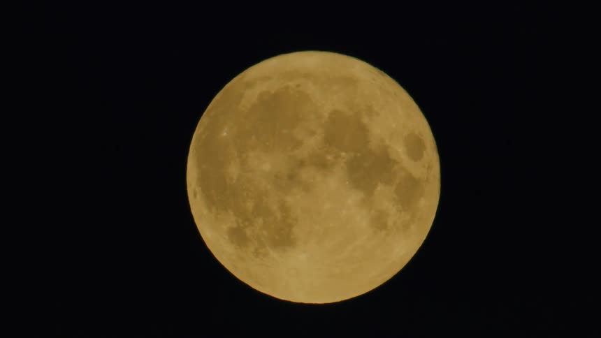 Yellowish full moon standing out against the night sky