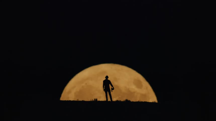 Silhouette of a person in front of the full moon rising on the night horizon