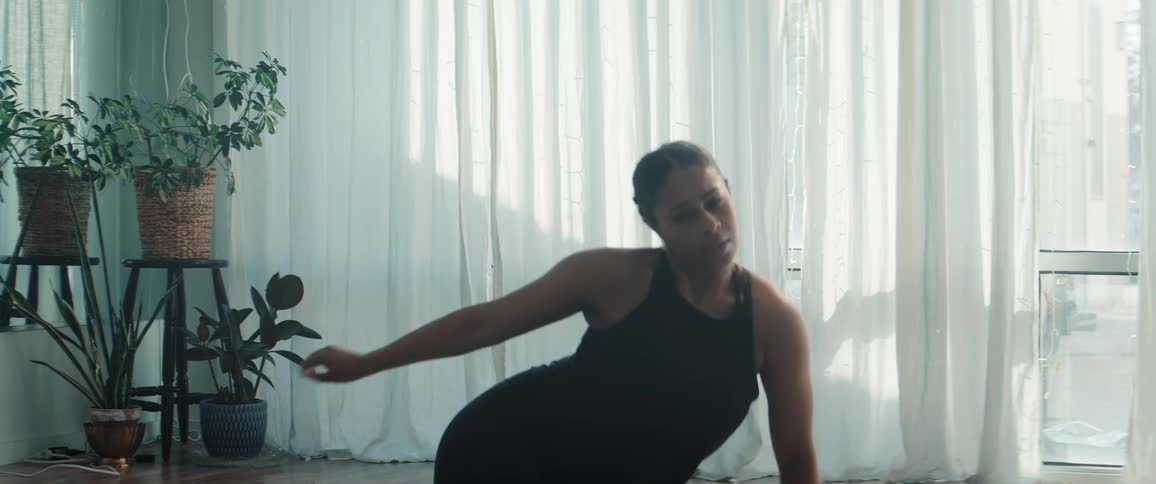 Woman performing a dance move in a studio lit by natural light next to plants