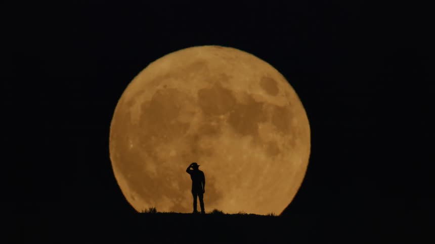 The man puts on his cowboy hat in front of the yellow moon