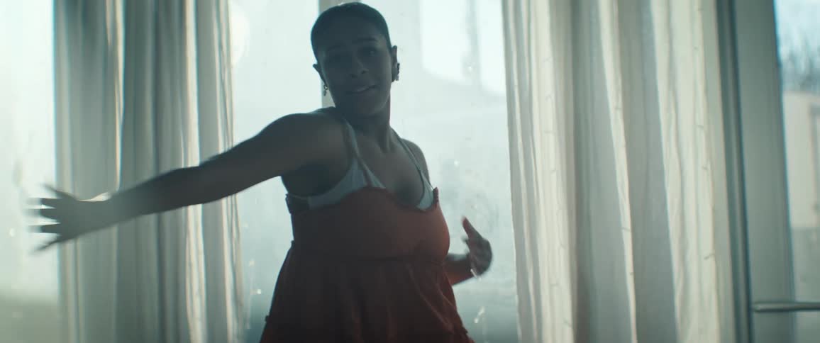 The woman reaches her arms up as she dances by the window