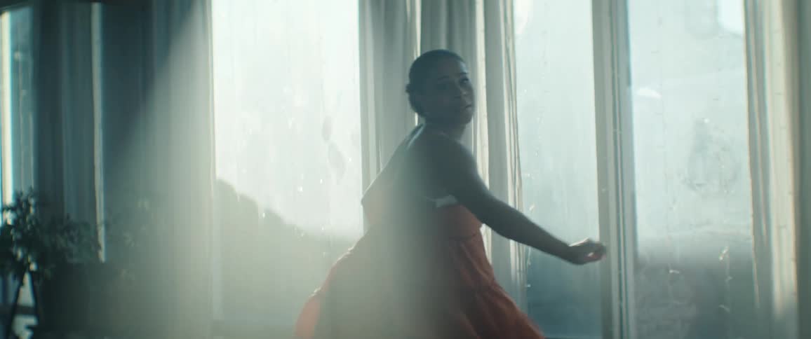 Woman in an orange dress dancing near a window lit by natural light