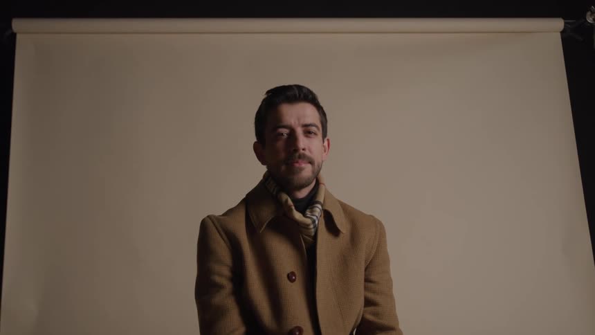 Man sitting in a brown coat and scarf against a neutral background