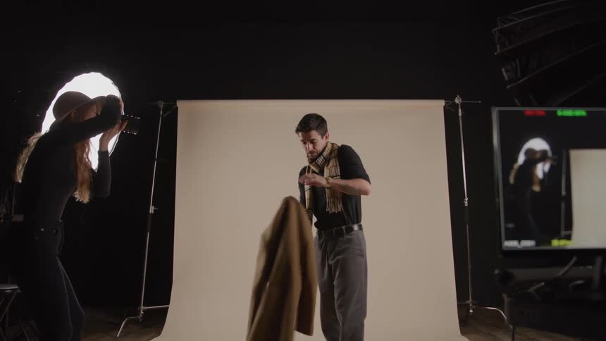 A man poses for a photographer with lights and a backdrop in a studio