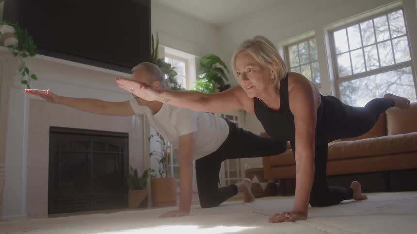 A middle aged couple stretching while doing yoga together on the floor in a living room during daytime