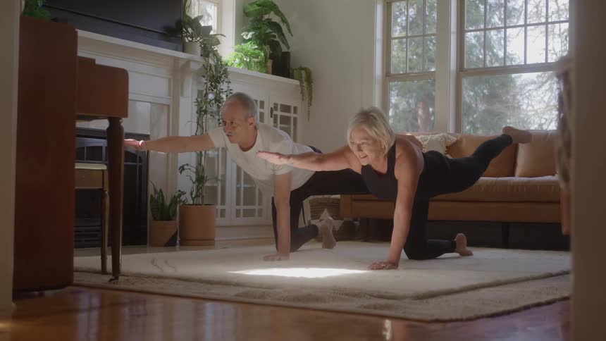 A couple practices yoga on a mat spread in their living room at midday