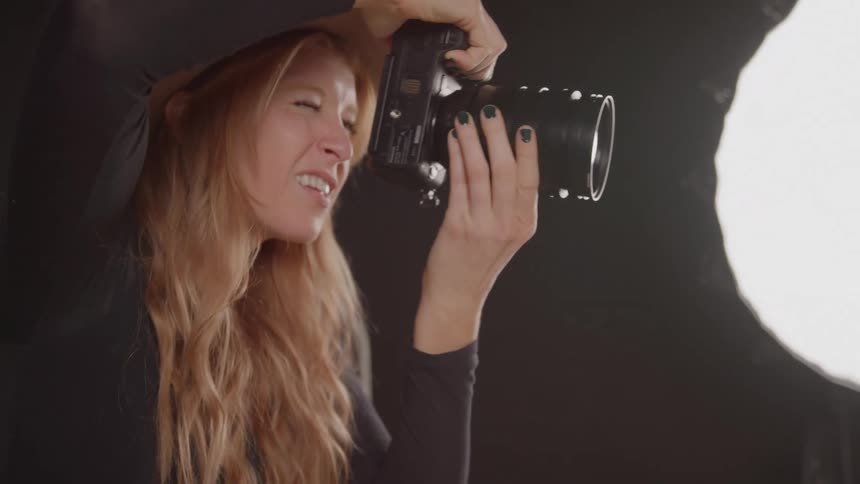 Young woman wearing a hat taking a picture indoors using an analog camera