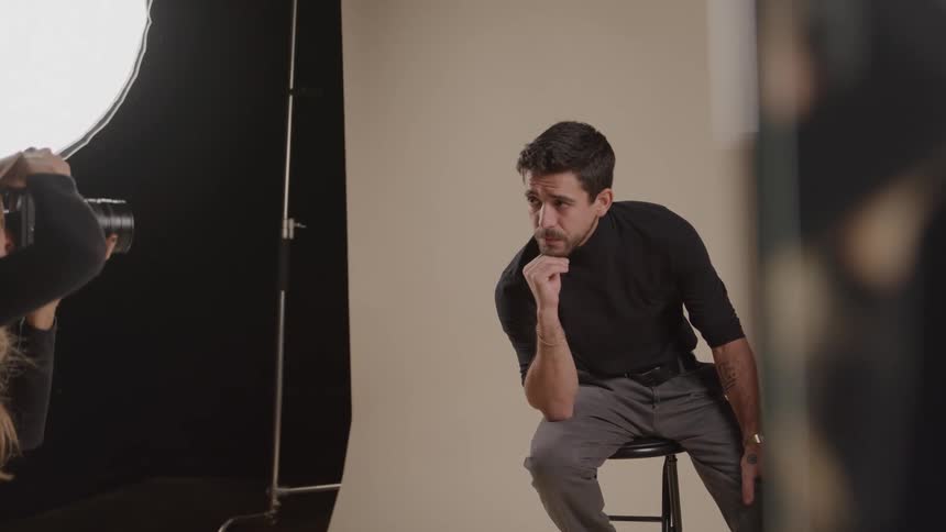 A young female photographer taking photos of a young man posing on a chair in a photo studio