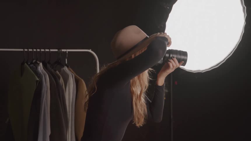Woman wearing a hat captures shots positioned in the studio beside clothing racks