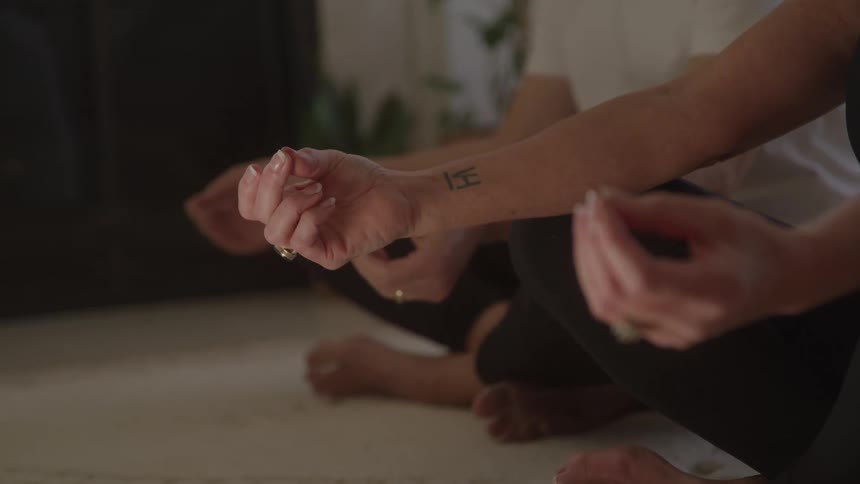 A man and a woman sit on the floor indoors meditating together