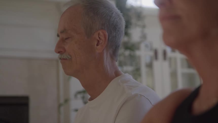 Man practices meditation with closed eyes next to a woman