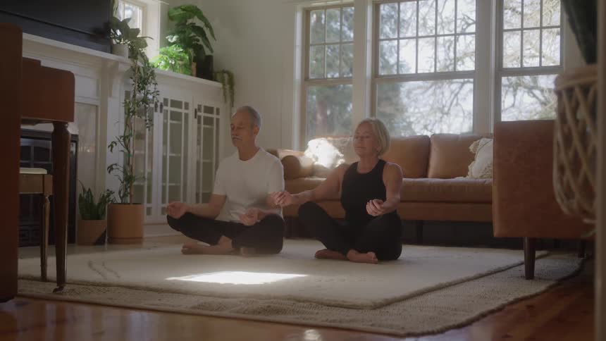 Couple seated on the rug practices yoga together in a bright living room