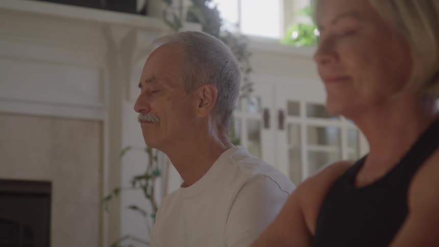 Mature couple practices yoga side by side with serene expressions