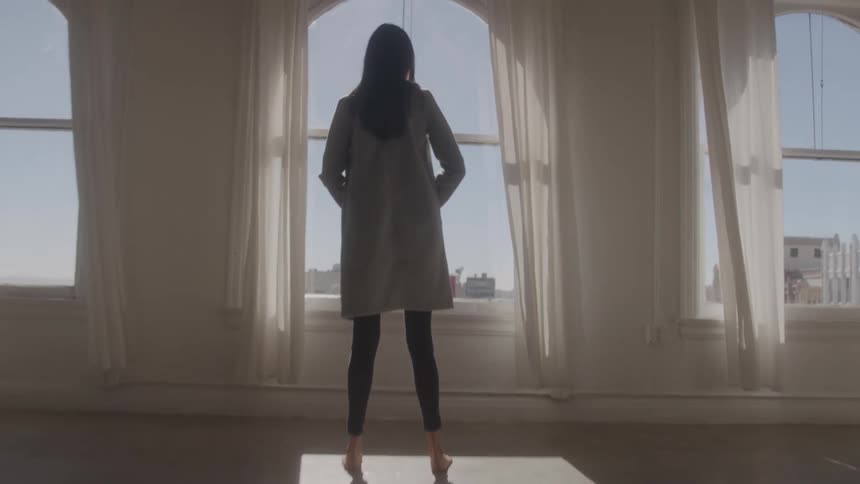 A young woman looking out through a window while standing in a corridor indoors during daytime