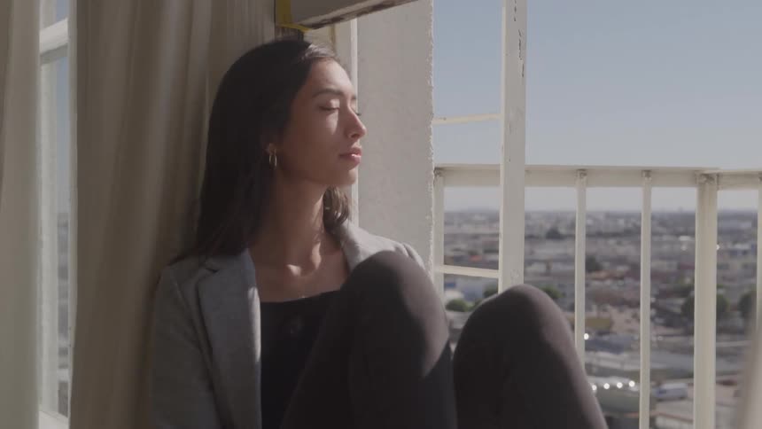 Close up of a young woman sitting contemplatively by a window in a room during daytime