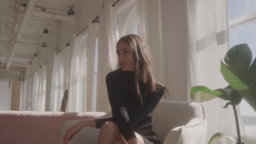 Woman sits near the window with a serene expression under natural light
