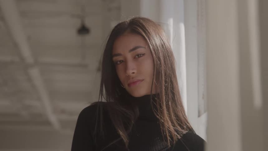 Woman poses with a soft gaze and confident expression near the window