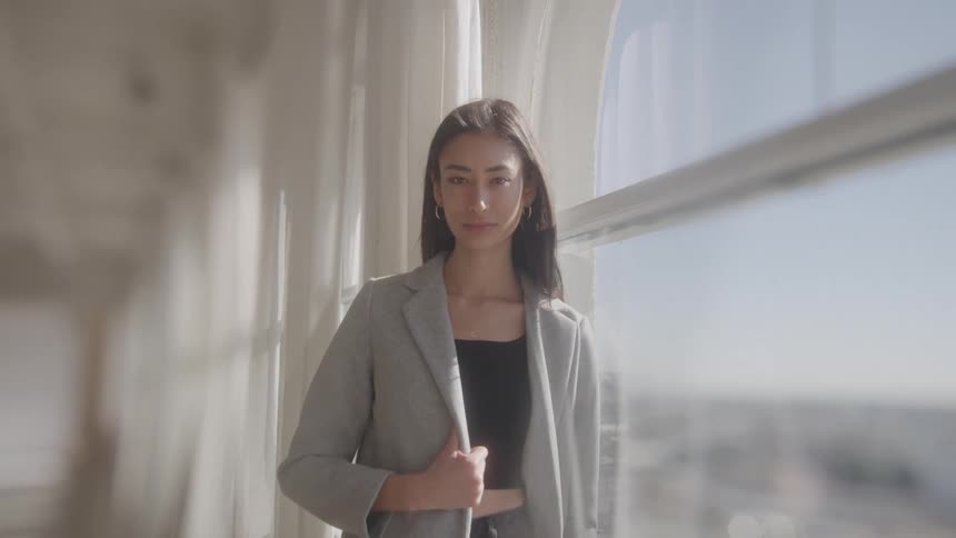 A young woman posing while wearing a formal fit as she stands by the corridor window during daytime