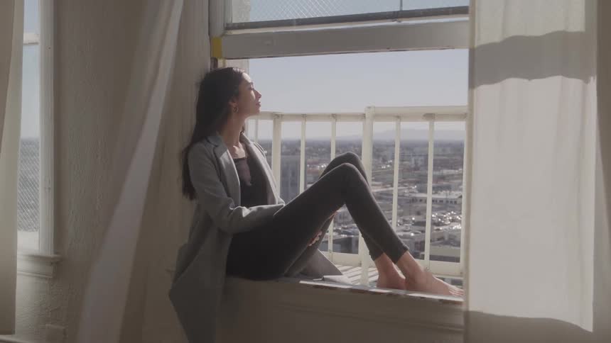 The woman is sitting on the windowsill overlooking the city