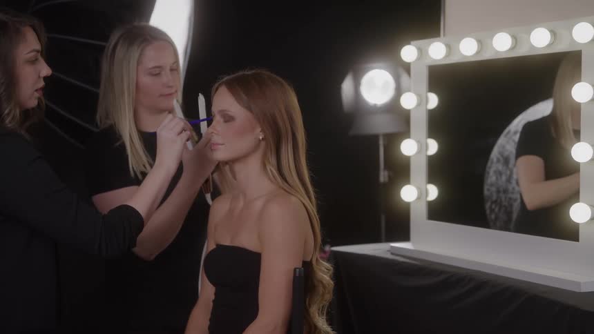 Woman sitting down having her makeup applied by two people