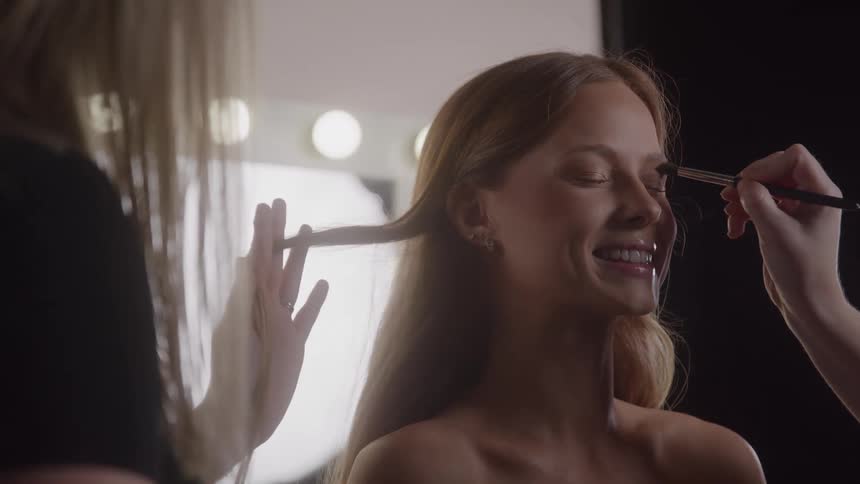 Model smiling widely while having her hair and makeup done