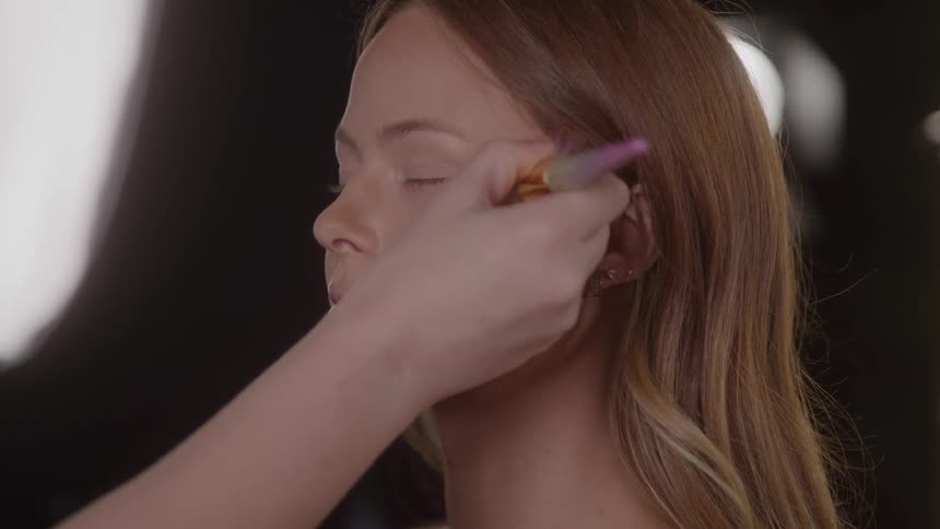 Woman gets makeup applied to her face with a brush in a welllit setting