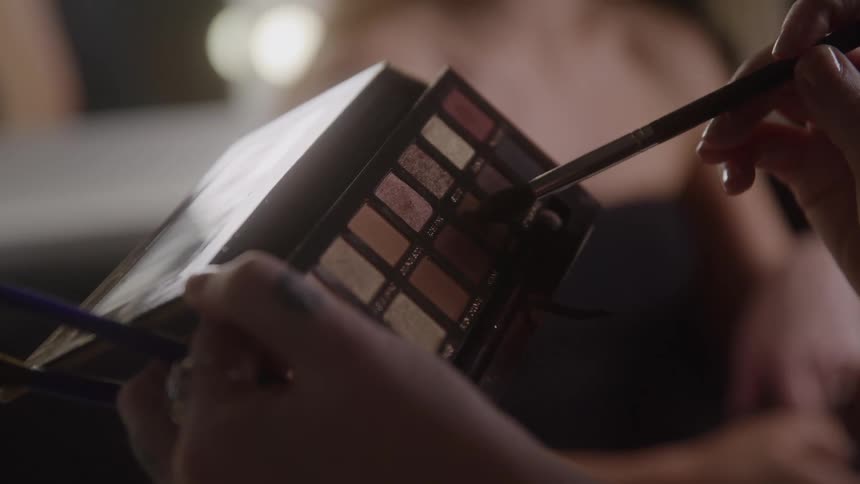 Hand holding a brush and selecting eyeshadow from a makeup palette