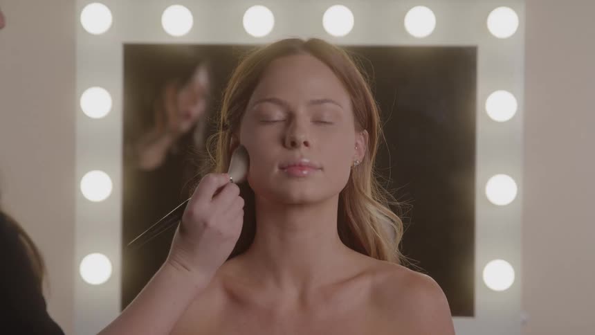 Makeup artist applying makeup on the face of a model with a brush indoors during day time