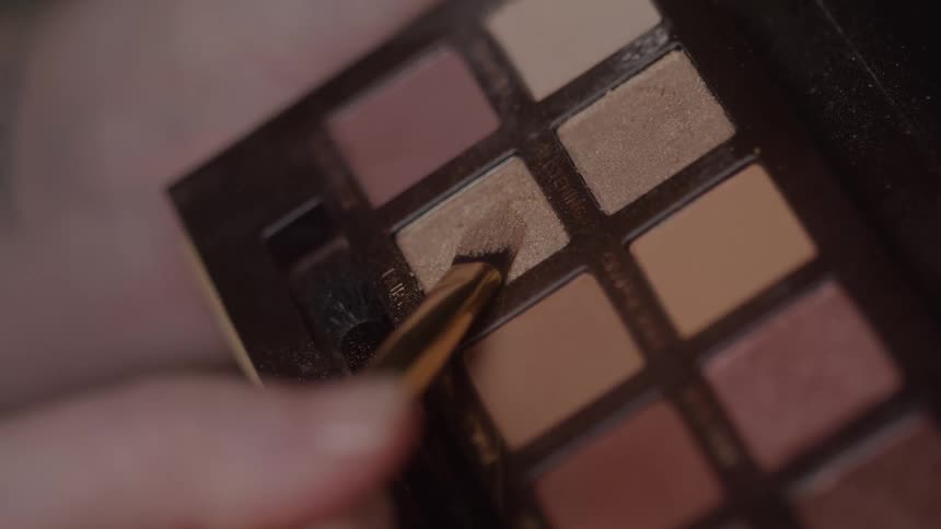 A person dabs a brush onto a makeup pallet