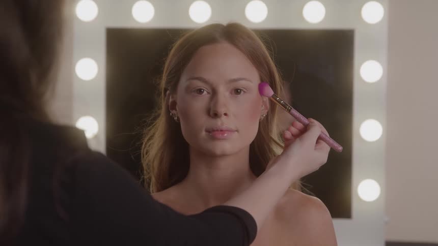 The woman uses a brush to apply makeup on the model