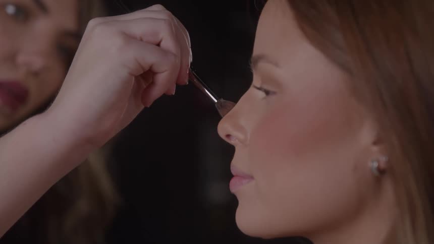 A woman has professional makeup applied by a beautician