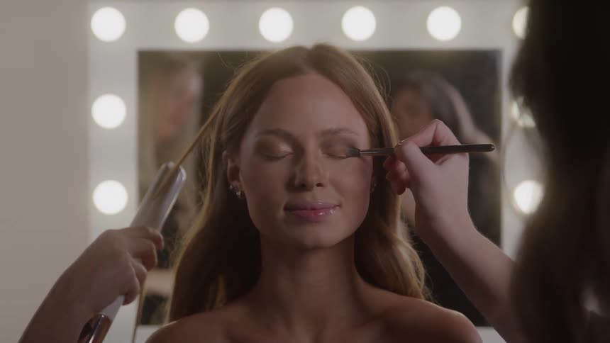Young female model having her hair done and makeup applied to her face indoors during day time