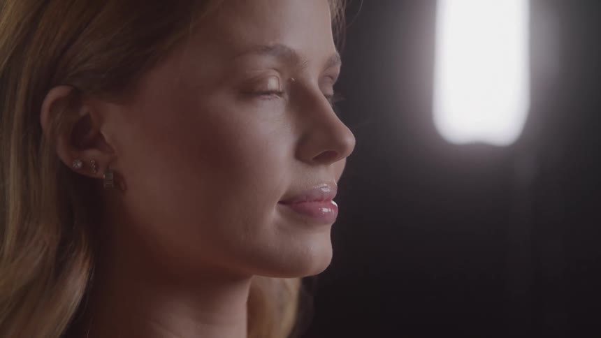 Makeup artist applying eye makeup to a light brownhaired woman with a dark backlit background
