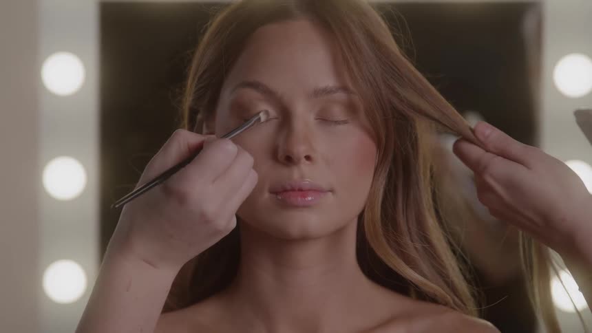 Young female model having her hair done and makeup applied to her face indoors