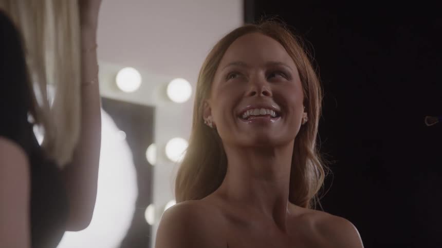 Woman smiling with light brown hair in front of a lighted mirror at sunset