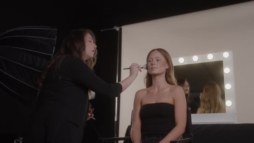 The make up artist is brushing the models face by the backdrop