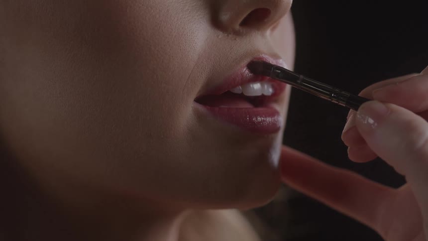 Brush applying lipstick to a persons lips in closeup