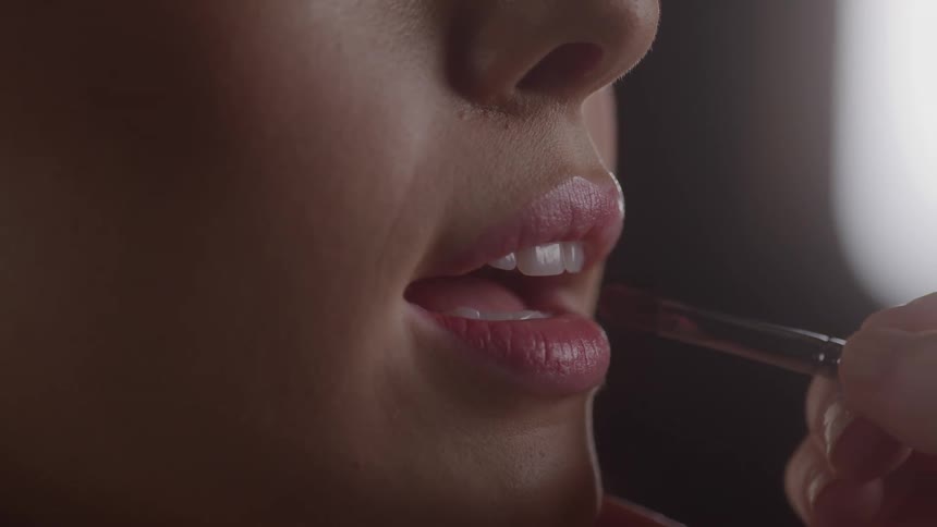 Woman applying lipstick with a brush on their lips