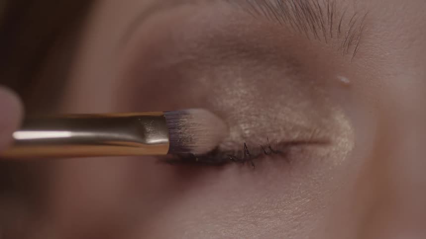Brush applying golden eyeshadow on a closed eyelid