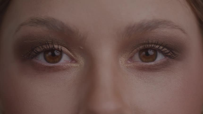 An extremely closeup shot focuses on a pair of eyes which are wide open and looking directly at the camera showing detailed eye makeup