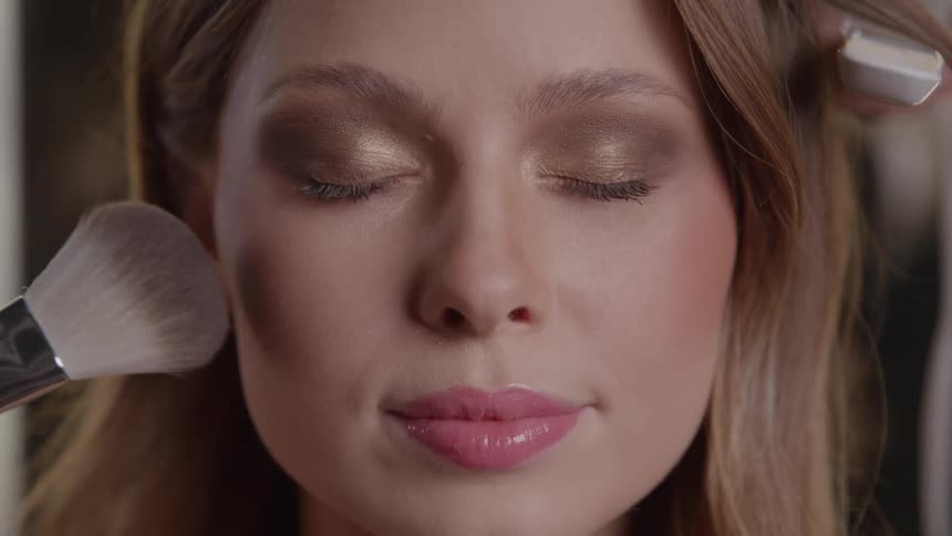 Woman with closed eyes receiving makeup and hairstyling simultaneously