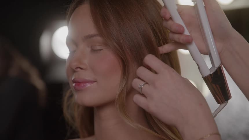 Light brown hair being styled with a curling iron by a professional in a welllit setting