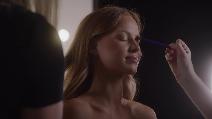 Person with closed eyes having makeup applied with a brush on the face