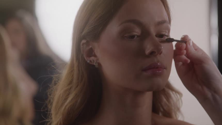 Makeup artist applying eyeliner to a light brownhaired woman in a professional setting