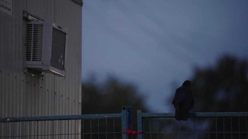 A black bird flies off a railing fence beside a building at midday