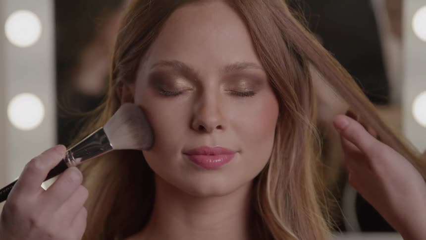 Woman with closed eyes having makeup and hairstyling done simultaneously