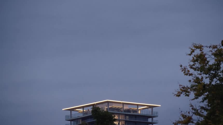 Modern building with glowing edges at dusk bird in flight and autumn trees in the background and crows flying through the frame