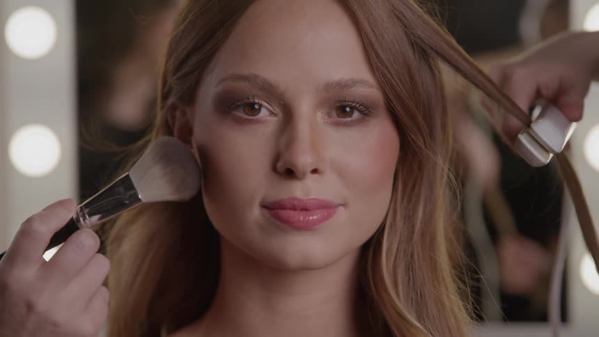 A woman gets her hair styled and makeup applied in a beauty studio