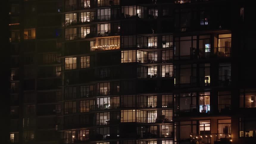 Residential building with lit windows showing varied interiors at night